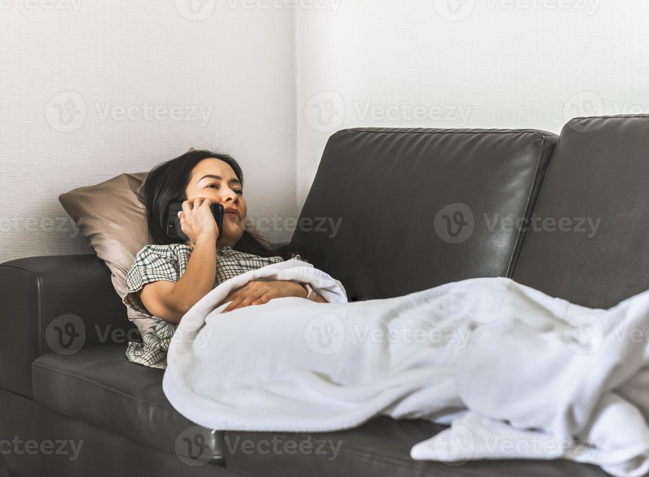 Frau, die auf einer Couch liegt, die auf Smartphone-Quarantänekonzept spricht foto