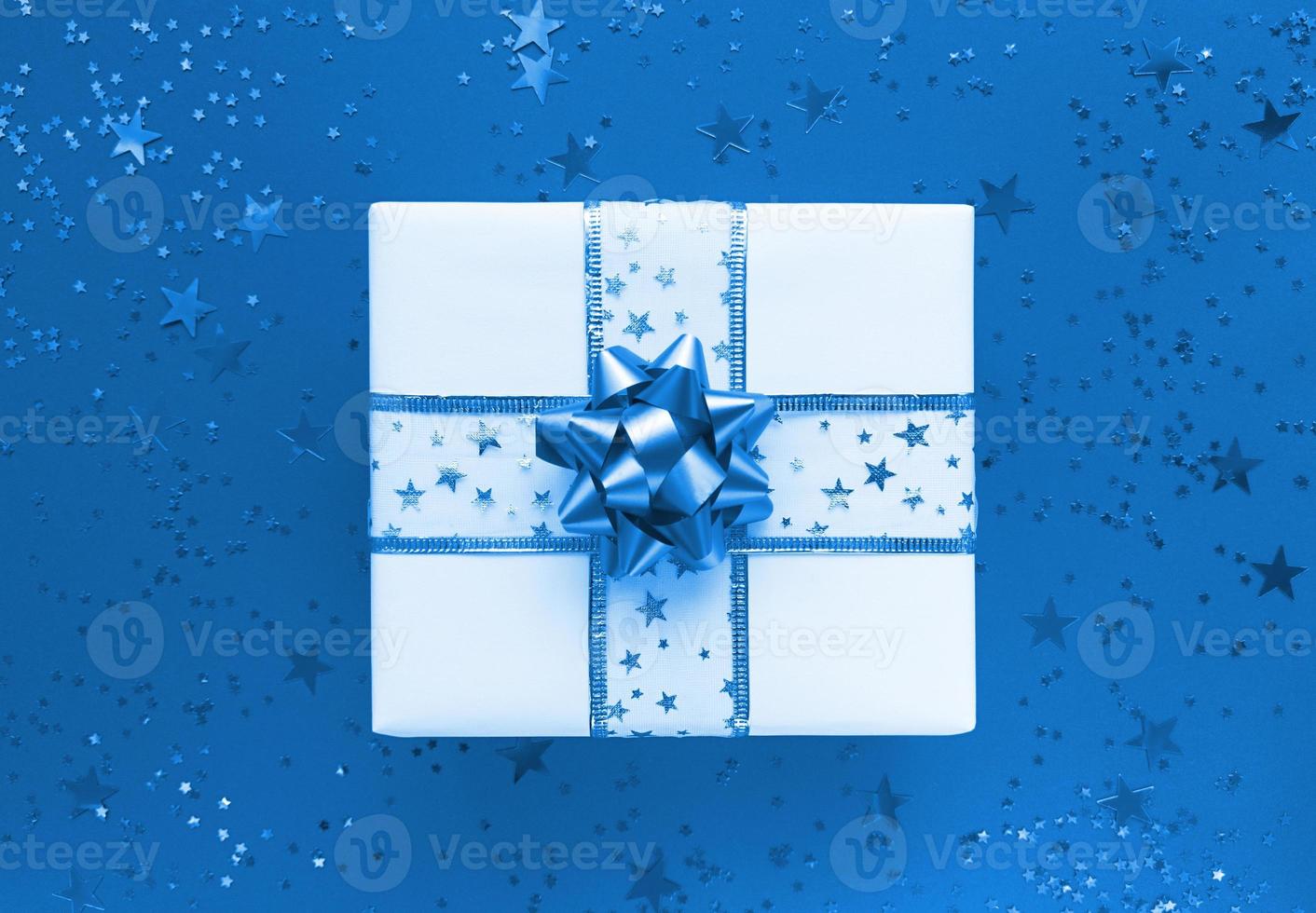 Geschenkbox und Sterne auf einem monochromen flachen Hintergrund des blauen Hintergrunds foto