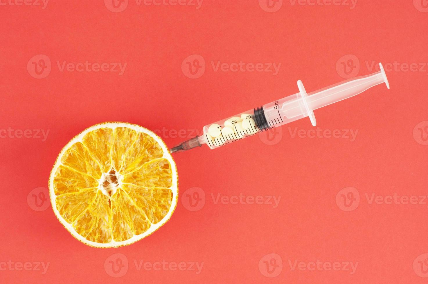 eine getrocknete Orange mit festsitzender Spritze auf rotem Hintergrund foto