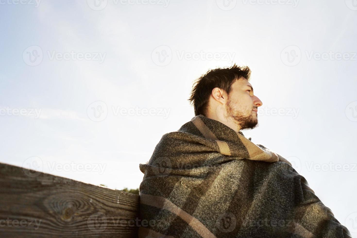 Seitengesicht eines jungen Mannes mit geschlossenen Augen, der in Ruhe die morgendliche Herbstsonne mit der Hintergrundbeleuchtung des blauen Himmels genießt foto