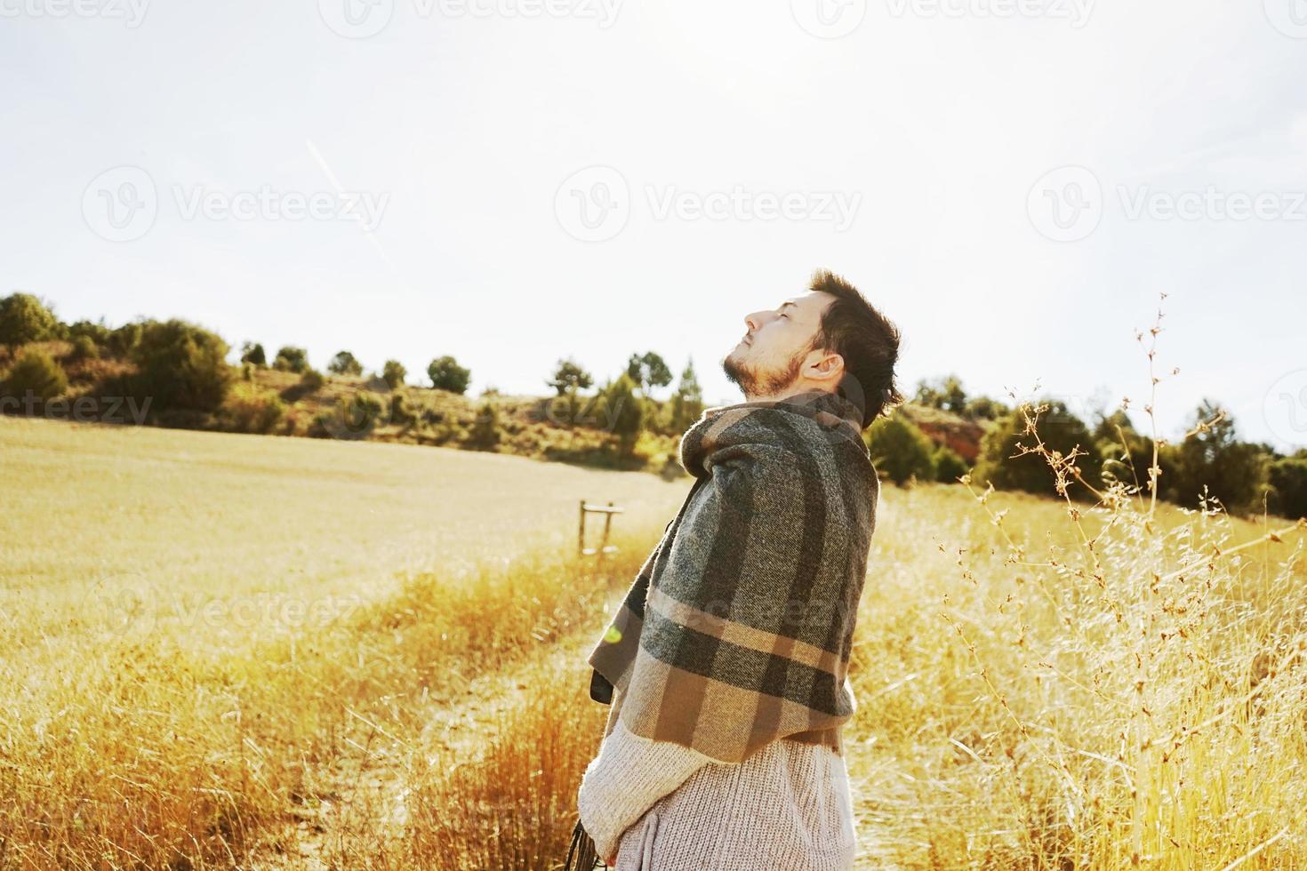 Seite eines Standes junger Mann, der in Ruhe die morgendliche Herbstsonne auf einem Weg eines gelben Feldes mit der Hintergrundbeleuchtung vom blauen Himmel genießt foto