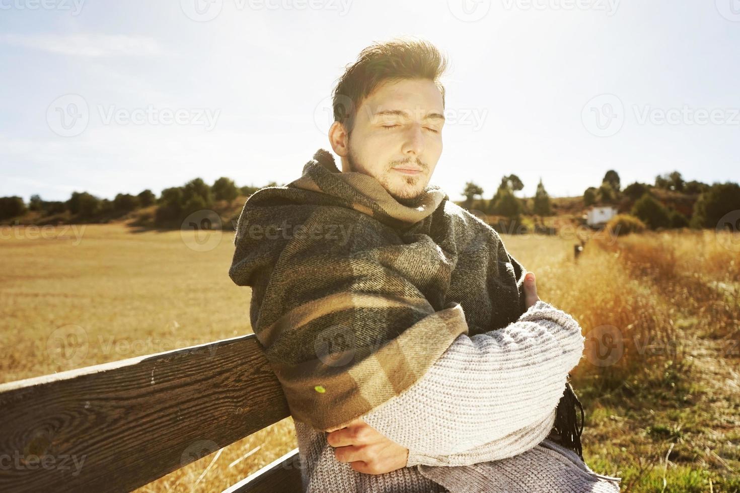 junger Mann mit geschlossenen Augen, der die morgendliche Herbstsonne mit der Hintergrundbeleuchtung vom blauen Himmel genießt foto