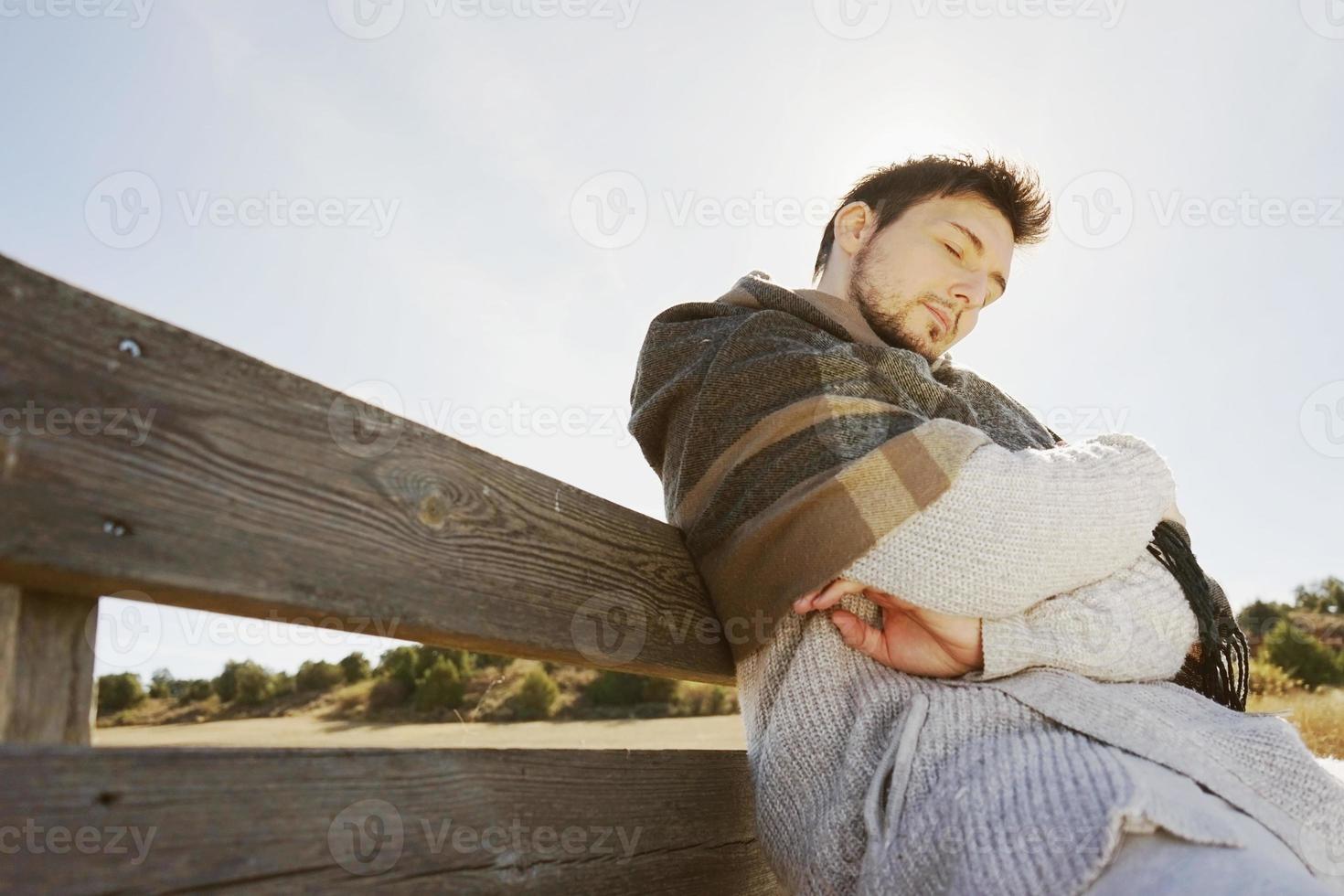 junger Mann, der die Morgenherbstsonne mit der Hintergrundbeleuchtung vom blauen Himmel schläft und genießt foto