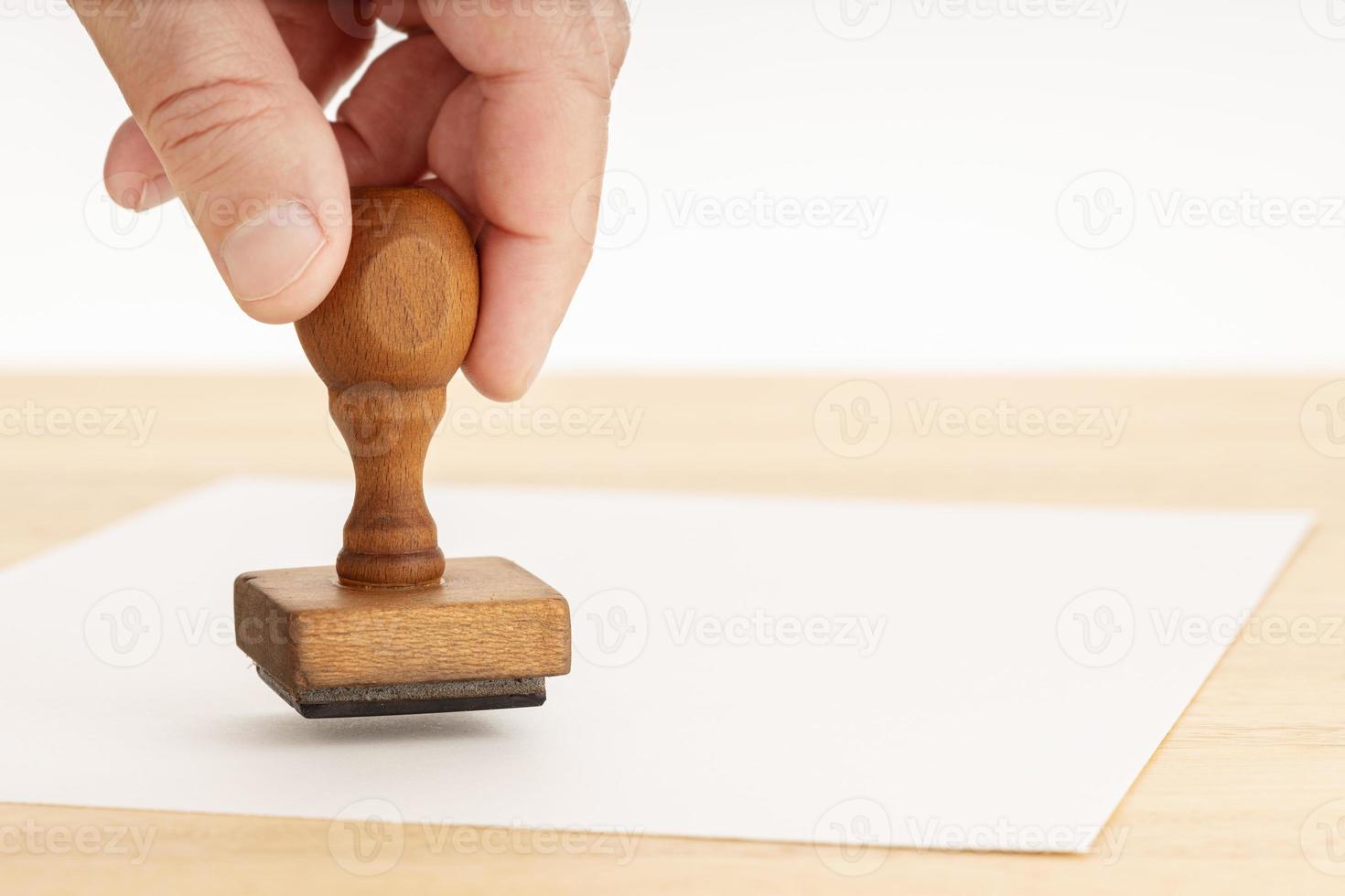 Hand hält einen Stempel und leeres Papier auf Holztisch foto