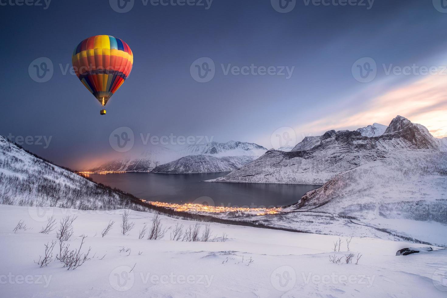 Heißluftballon, der auf Schneehügel mit Fordgardstadt im Winter fliegt foto