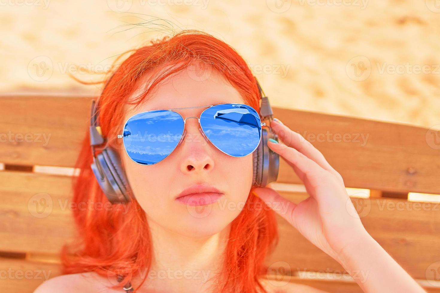 schöne Frau in der Sonnenbrille, die Musik am Strand hört foto