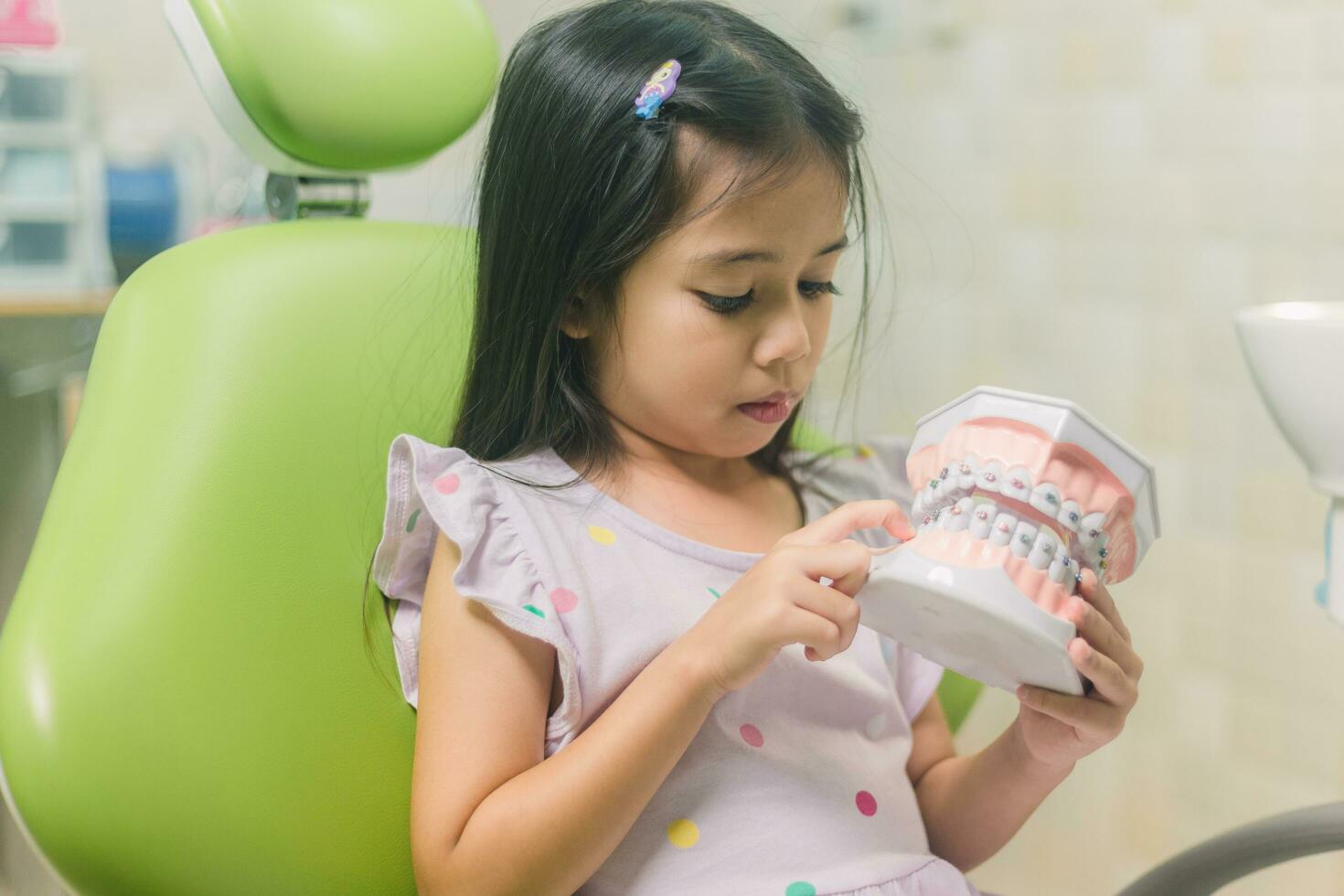 asiatisch Mädchen im Dental Stuhl, mit Zahn Bürste. Medizin, Zahnheilkunde und Gesundheitswesen Konzept foto