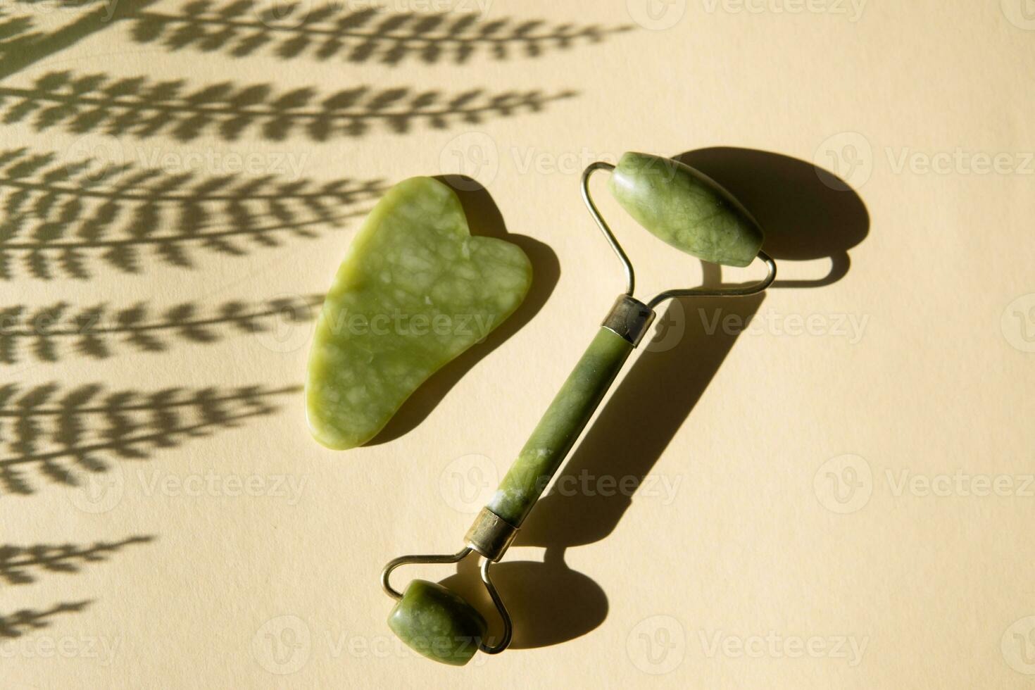 Jade gua sha Schaber und Gesicht Walze Massagegerät auf ein Kork runden Stand mit ein Monstera Blatt. foto