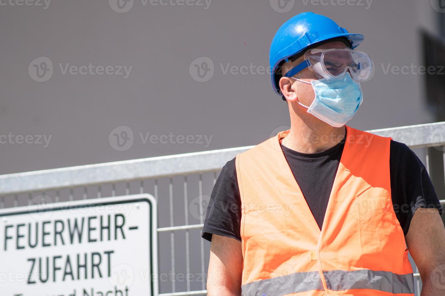 Bauarbeiter mit blauem Schutzhelm, Warnweste und chirurgischer Schutzmaske foto