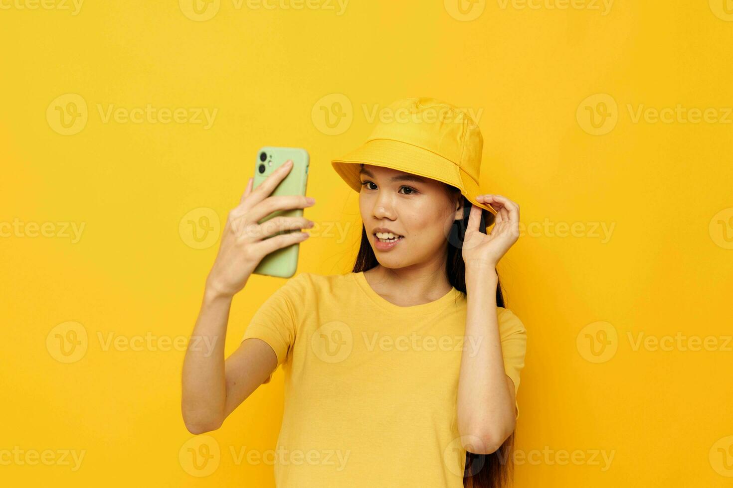 Frau mit asiatisch Aussehen im ein Gelb Hut und T-Shirt reden auf das Telefon Gelb Hintergrund unverändert foto