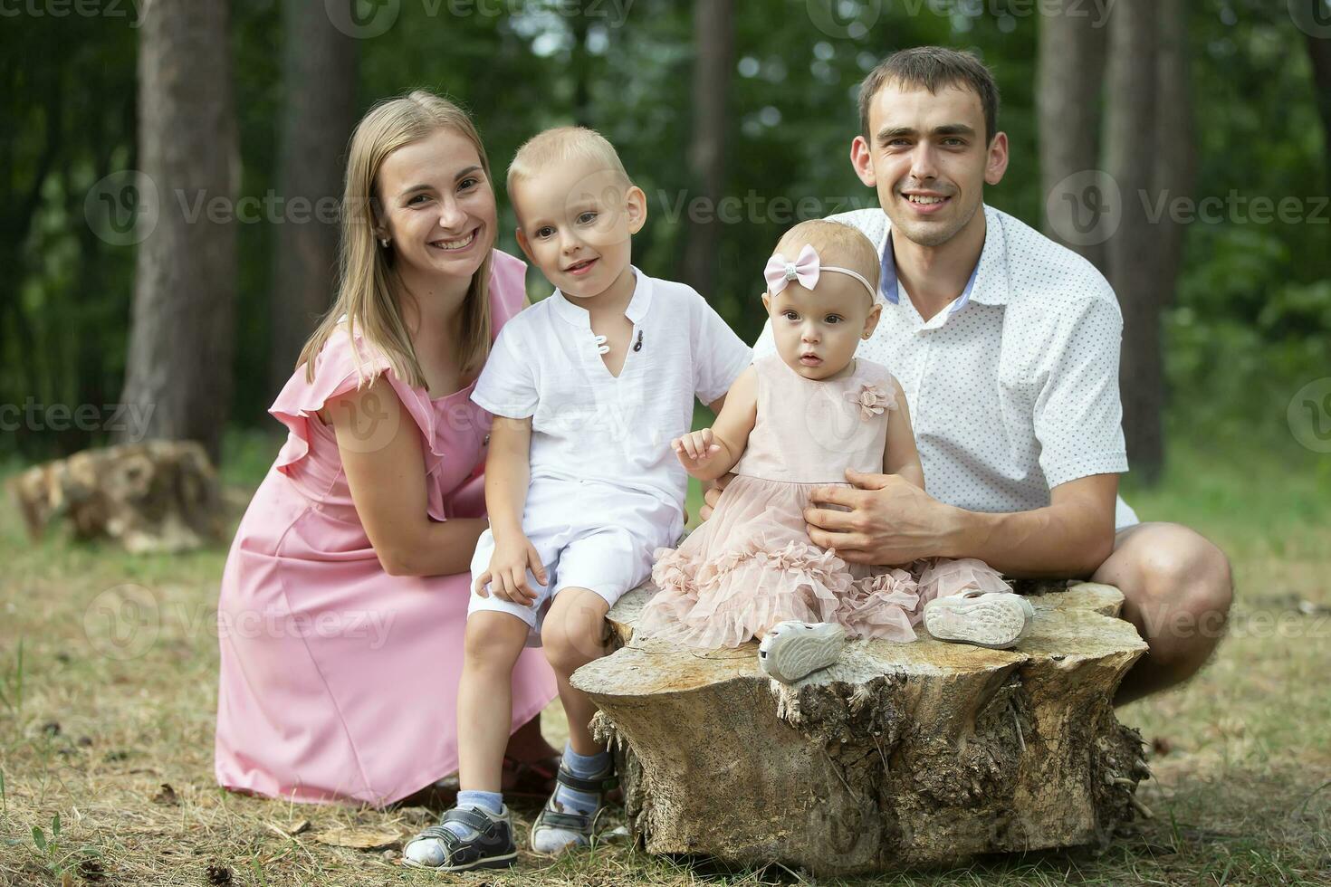 Mann und Ehefrau und ihr wenig Kinder. Familie Porträt im Natur. Mama und Papa sind posieren mit ihr Bruder und Schwester. jung Familie mit Kinder zum ein gehen im das Wald. foto