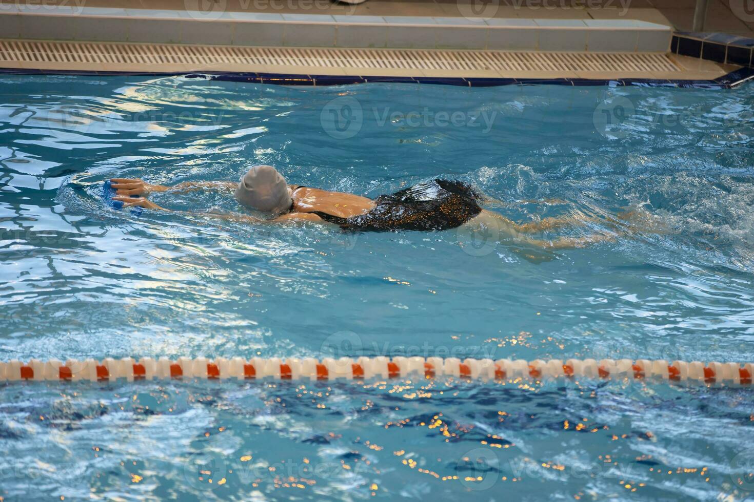 ein Frau schwimmt im ein schwarz Badeanzug und ein Schwimmen Deckel schwimmt im das Schwimmbad. foto