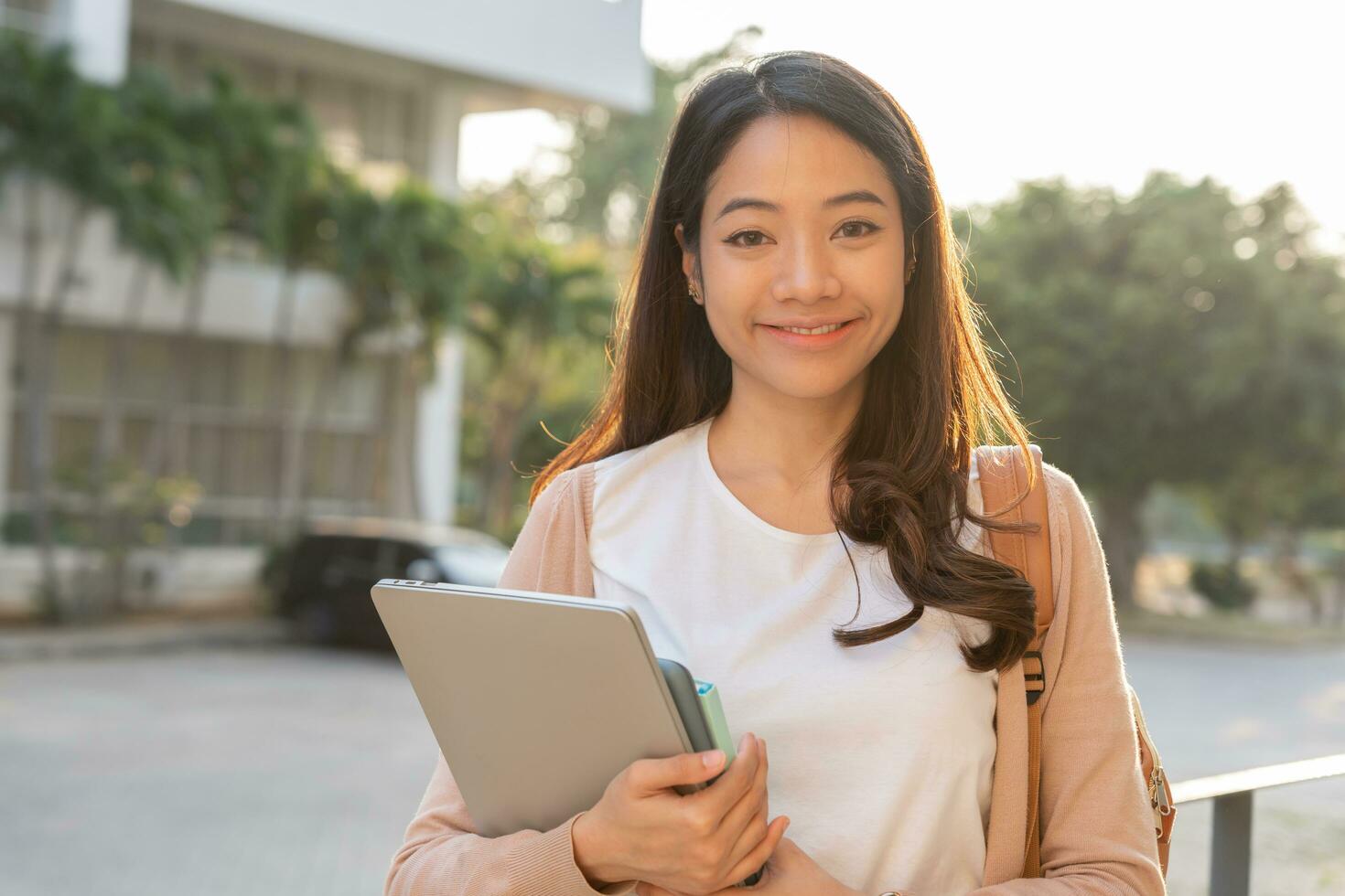 schöne asiatische Studentin mit Rucksack und Büchern im Freien. lächelndes Mädchen, das glücklich ist, viel Buch auf dem College-Campus zu tragen. Porträtfrau an der International Asia University. Bildung, Studium, Schule foto