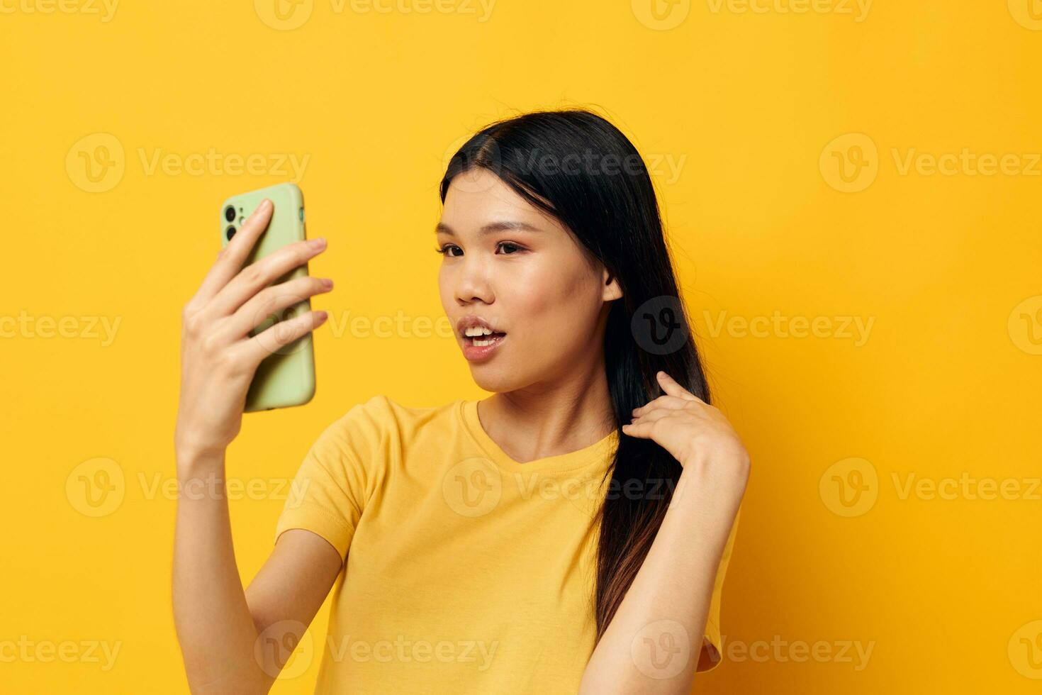 ziemlich Brünette im ein Gelb T-Shirt suchen beim das Telefon posieren isoliert Hintergrund unverändert foto