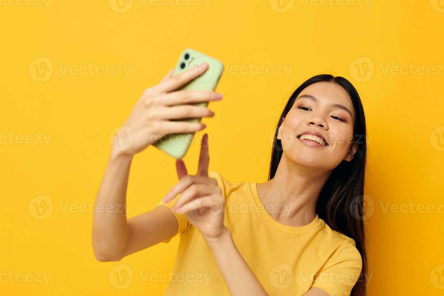 Frau mit asiatisch Aussehen mit ein Telefon im ihr Hände macht ein Selfie Studio Modell- unverändert foto