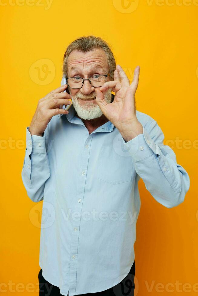 Foto von im Ruhestand alt Mann im ein Blau Hemd und Brille reden auf das Telefon Gelb Hintergrund