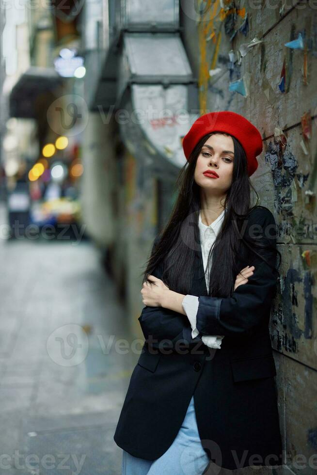 Mode Frau Porträt Gehen Tourist im stilvoll Kleider mit rot Lippen Gehen Nieder ein eng Stadt Straße, reisen, filmisch Farbe, retro Jahrgang Stil, dramatisch gegen ein Mauer mit Graffiti. foto