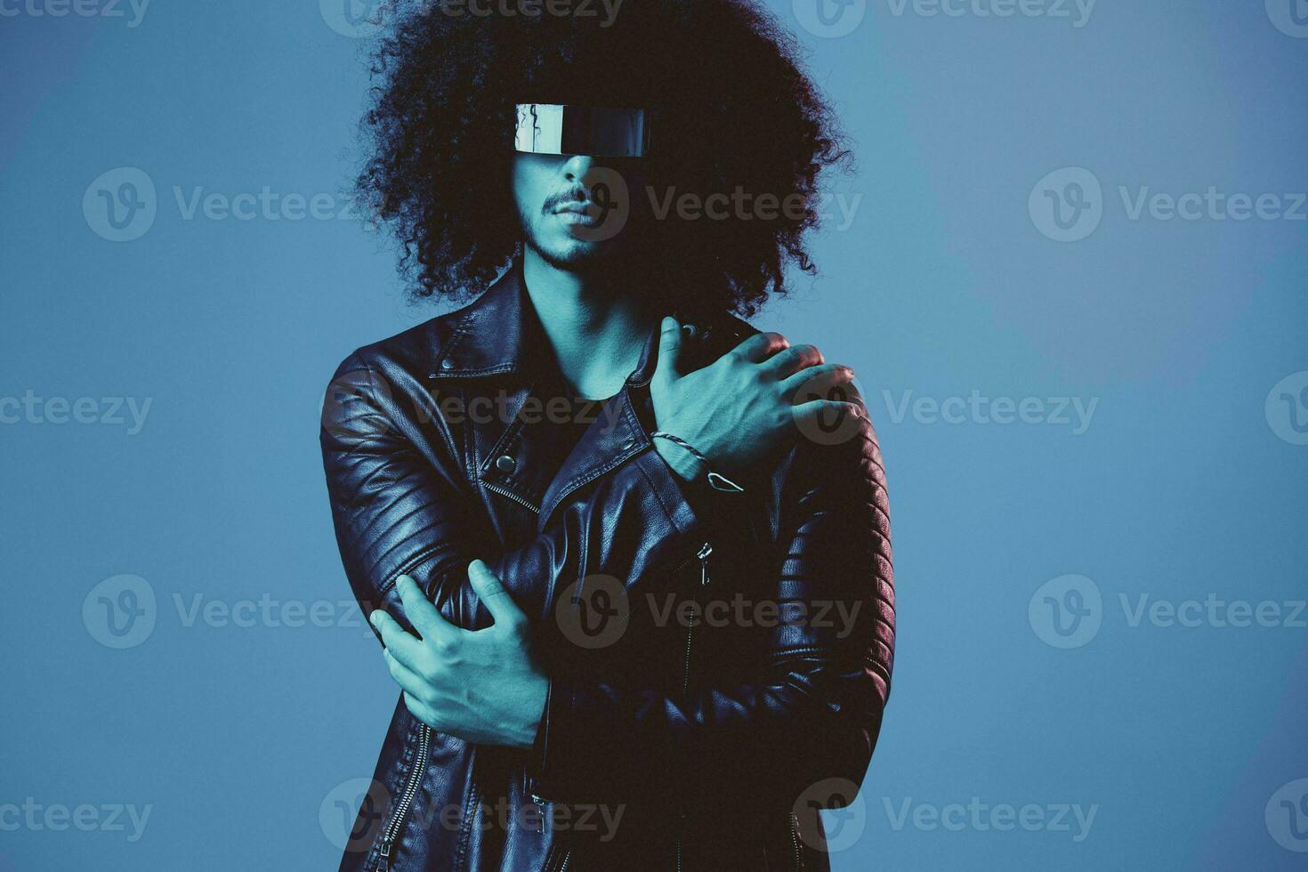 Porträt von Mode Mann mit lockig Haar mit stilvoll Brille auf Blau Hintergrund multinational, farbig Licht, schwarz Leder Jacke Trend, modern Konzept. foto