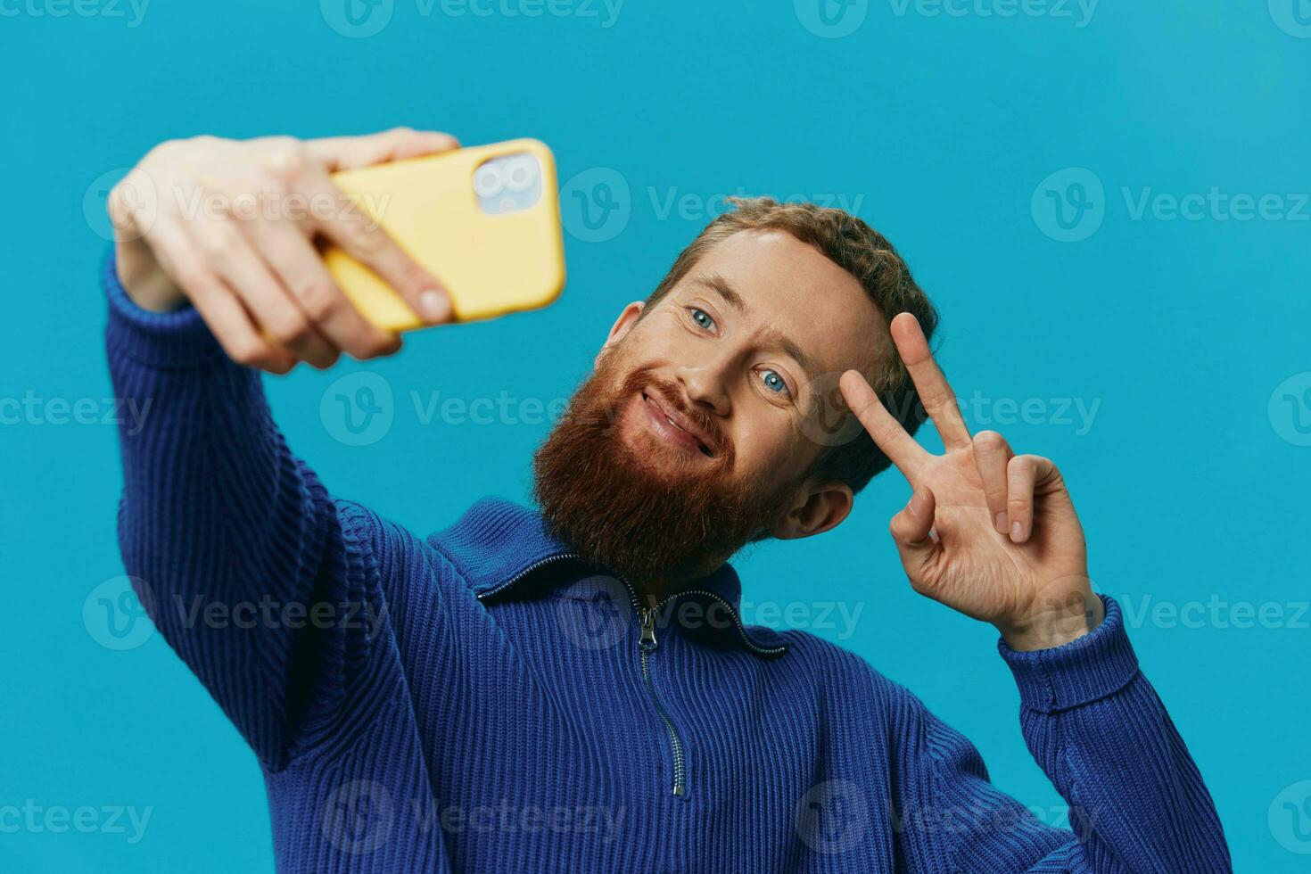 Porträt von ein Mann mit ein Telefon im seine Hände Blogger nimmt Selfies, auf ein Blau Hintergrund. kommunizieren online Sozial Medien, Lebensstil foto