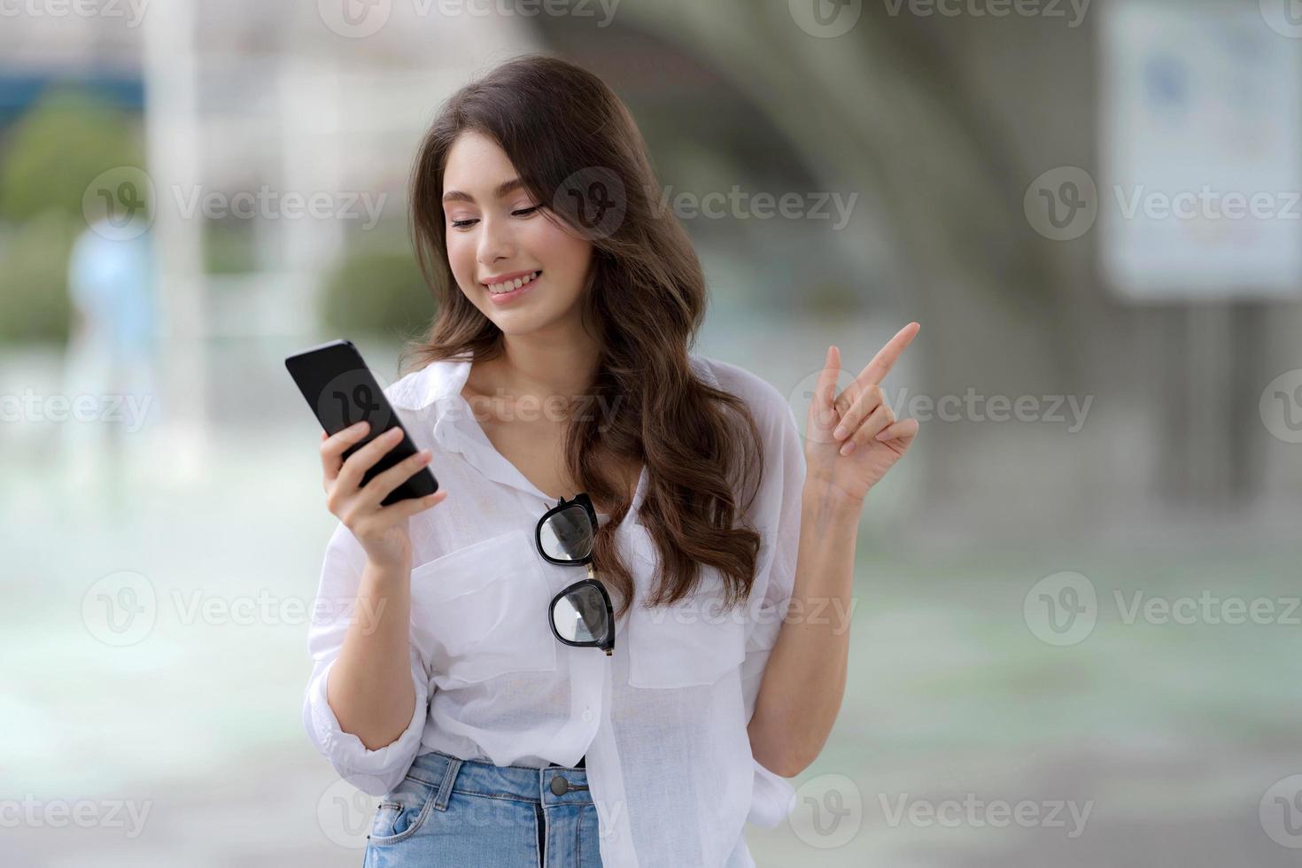 Porträt der jungen Frau mit Smiley-Gesicht unter Verwendung eines Telefons geht in einer Stadt foto