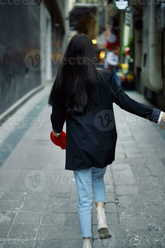 Mode Frau Tourist im stilvoll Kleider im ein Jacke und rot Baskenmütze Laufen Nieder das eng Straße von das Stadt Lächeln und Glück Reise, Französisch Stil, filmisch Farbe. foto
