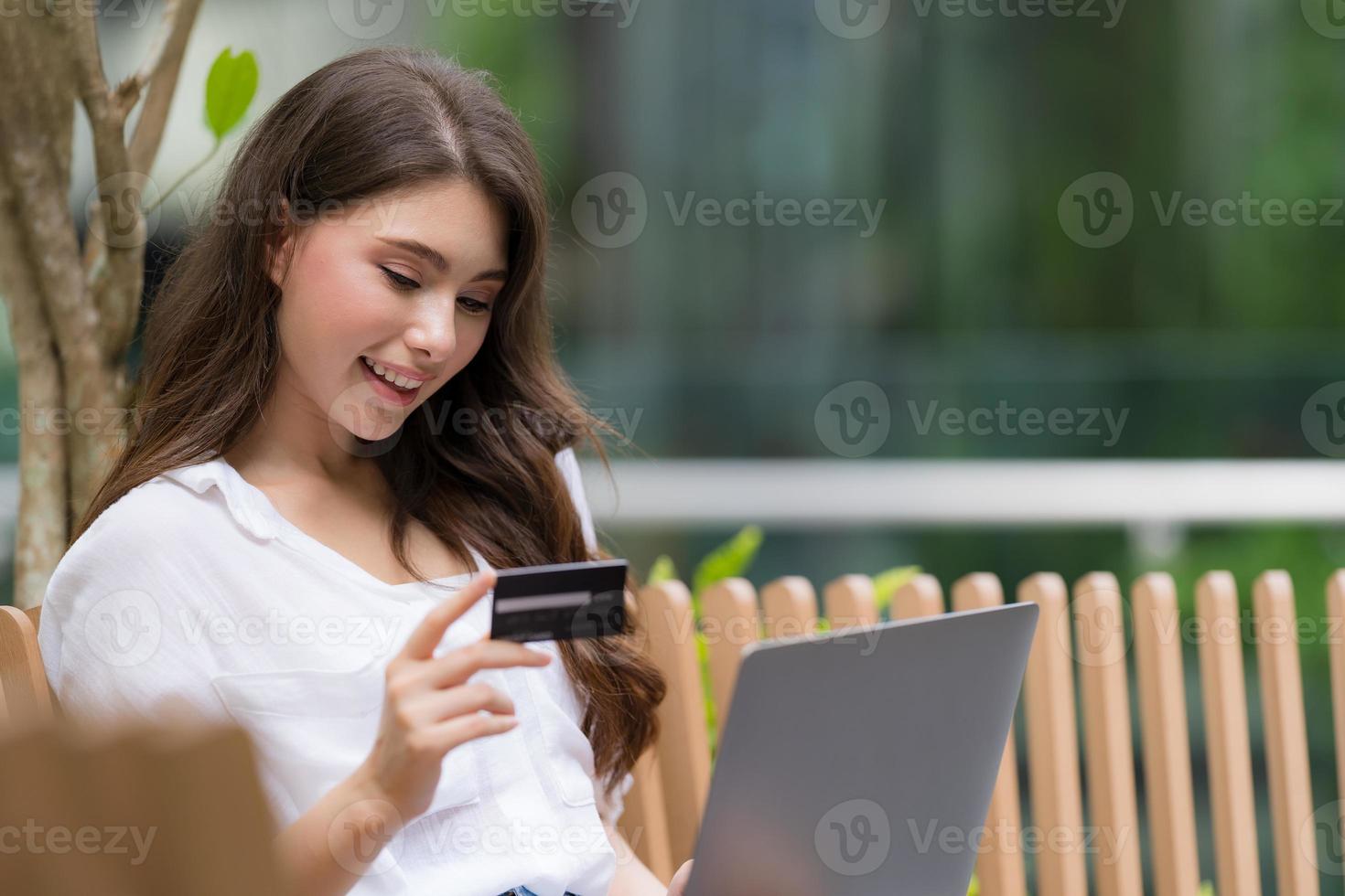 junge Frau, die auf einem Stuhl im Stadtpark unter Verwendung des Laptops sitzt foto