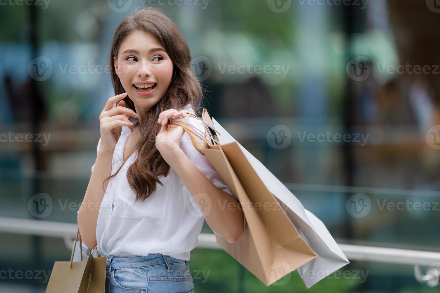 Außenporträt der glücklichen Frau, die Einkaufstaschen und lächelndes Gesicht hält foto