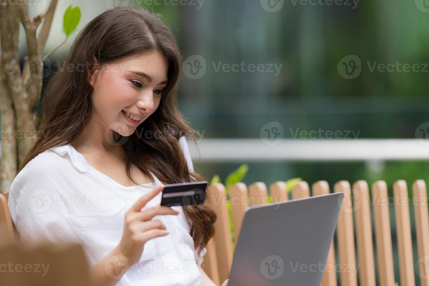 junge Frau, die auf einem Stuhl im Stadtpark unter Verwendung des Laptops sitzt foto