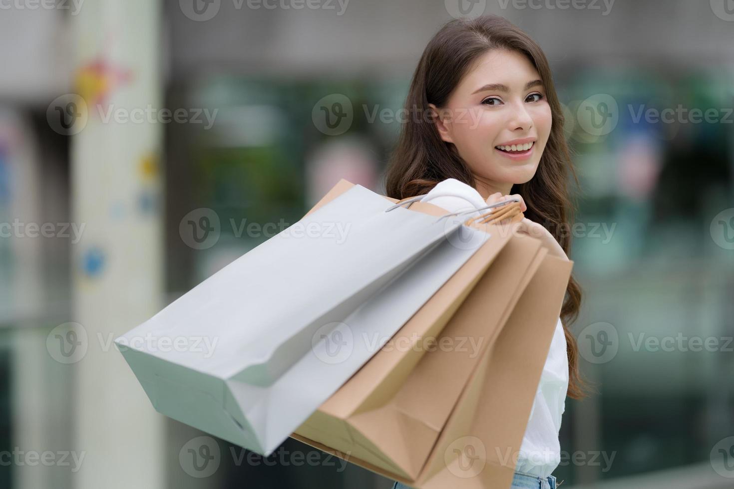 Außenporträt der glücklichen Frau, die Einkaufstaschen und lächelndes Gesicht hält foto