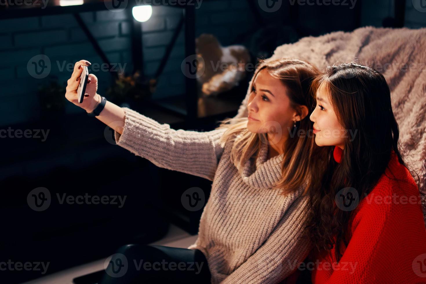 Zwei süße Mädchen in Strickpullovern machen Selfies auf dem Smartphone foto