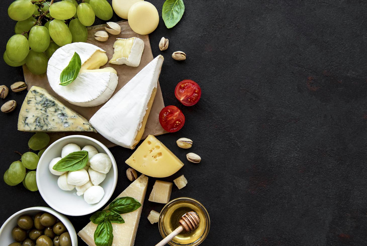 verschiedene Arten von Käse, Trauben, Honig und Snacks auf einem schwarzen Betonhintergrund foto