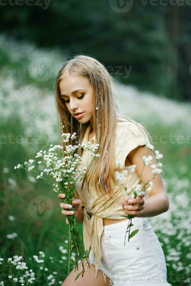 schön jung Frau pflücken Weiß Wildblumen auf das Hintergrund von ein Wald Landschaft im Sommer. Porträt von ein sanft glücklich Frau im ein wild Feld, genießen Natur. natürlich Schönheit Modell- foto