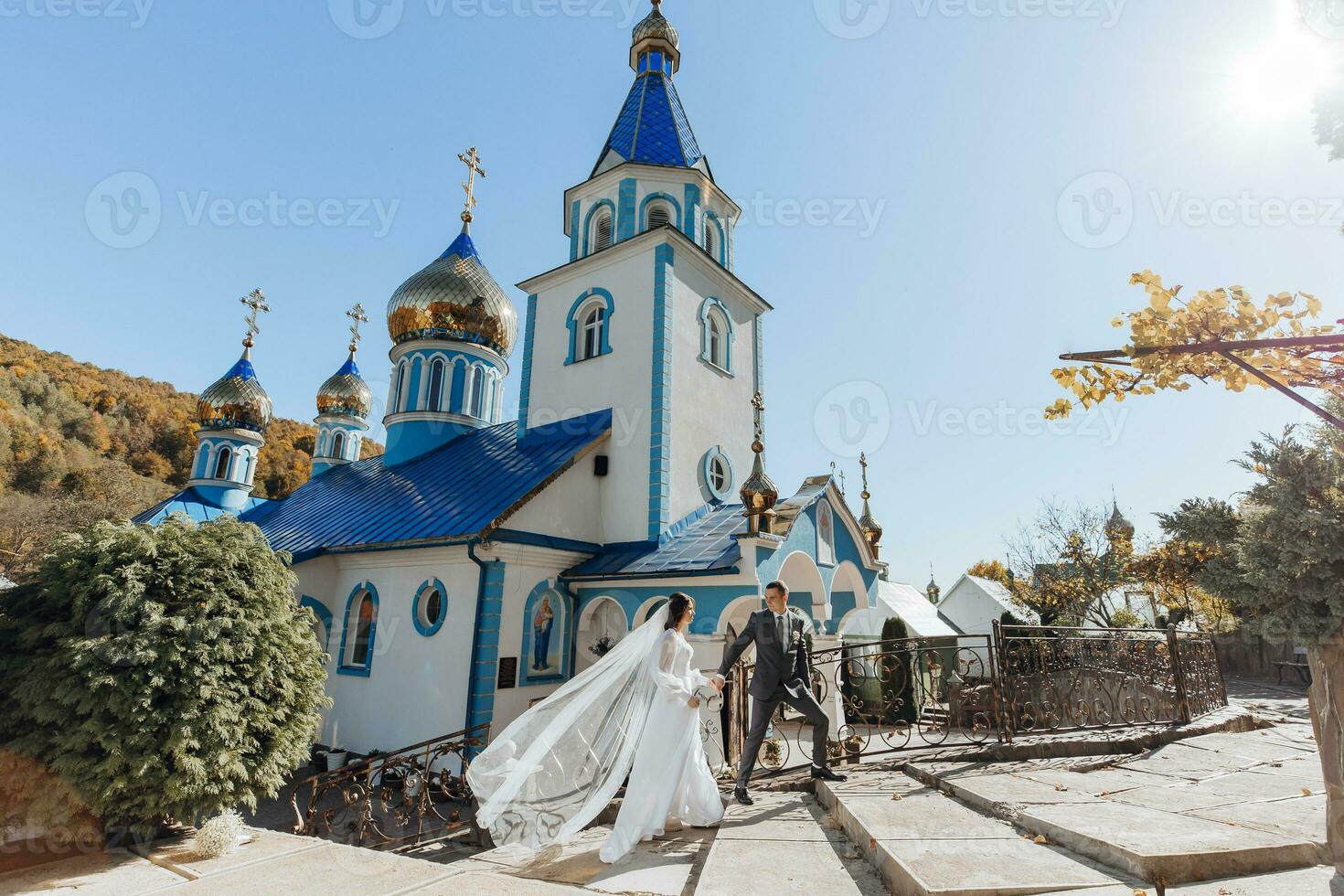 Hochzeit Tag. Bräutigam und Braut halten Hände und Gehen in der Nähe von das Kirche nach das Hochzeit Zeremonie. ein Paar von Jungvermählten im Liebe. unter das wunderbar Licht. Konzept von Hochzeit. foto