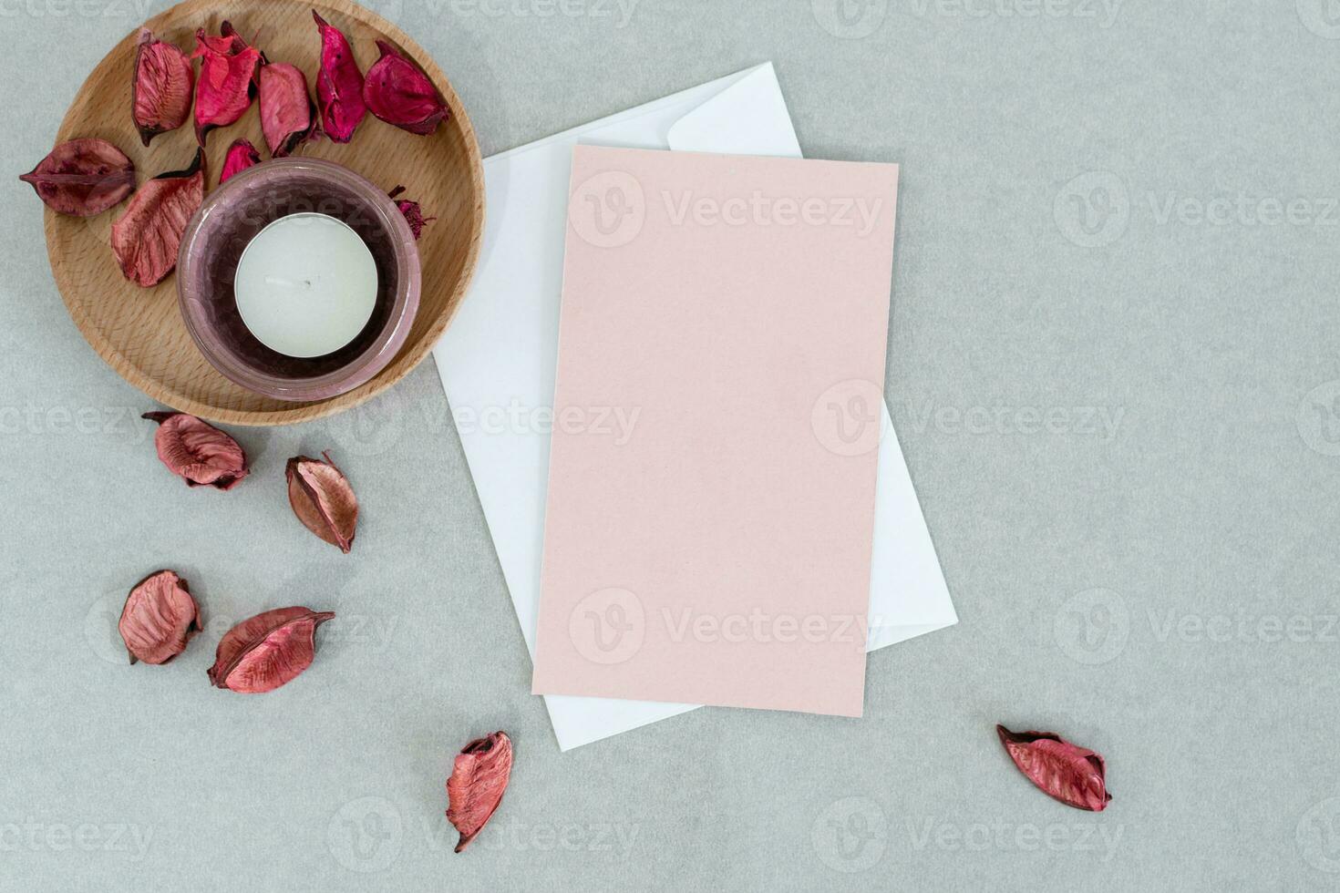 leeren Rosa Karte mit Weiß Umschlag, Kerze und Blütenblätter, auf grau Hintergrund. foto