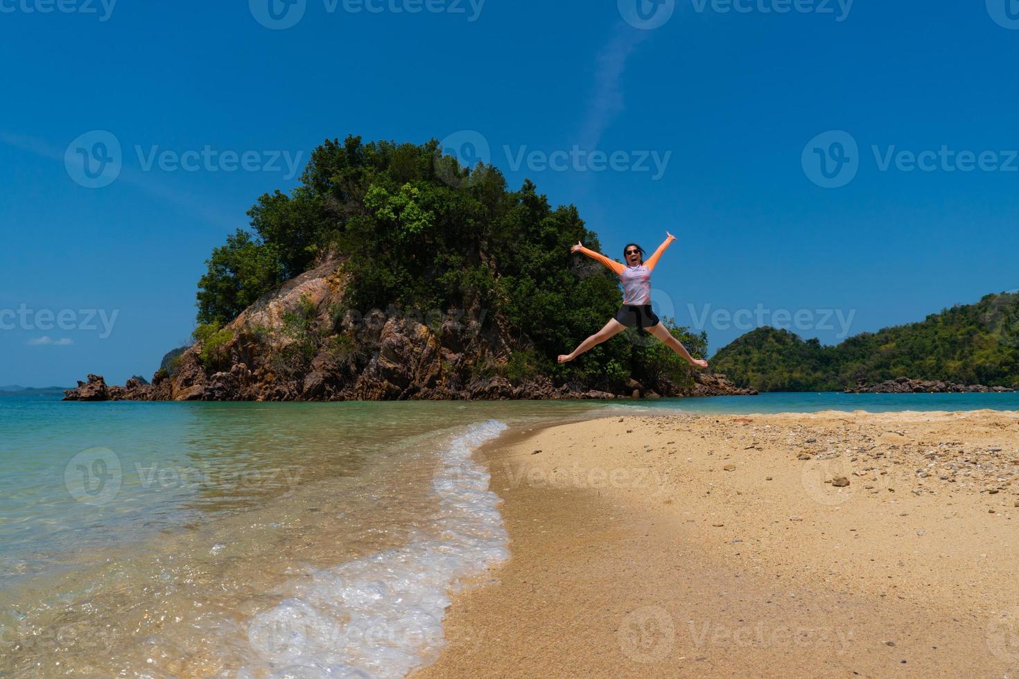 junge asiatische frau, die badeanzug trägt und im sommerurlaub am strand auf einer kleinen insel springt foto