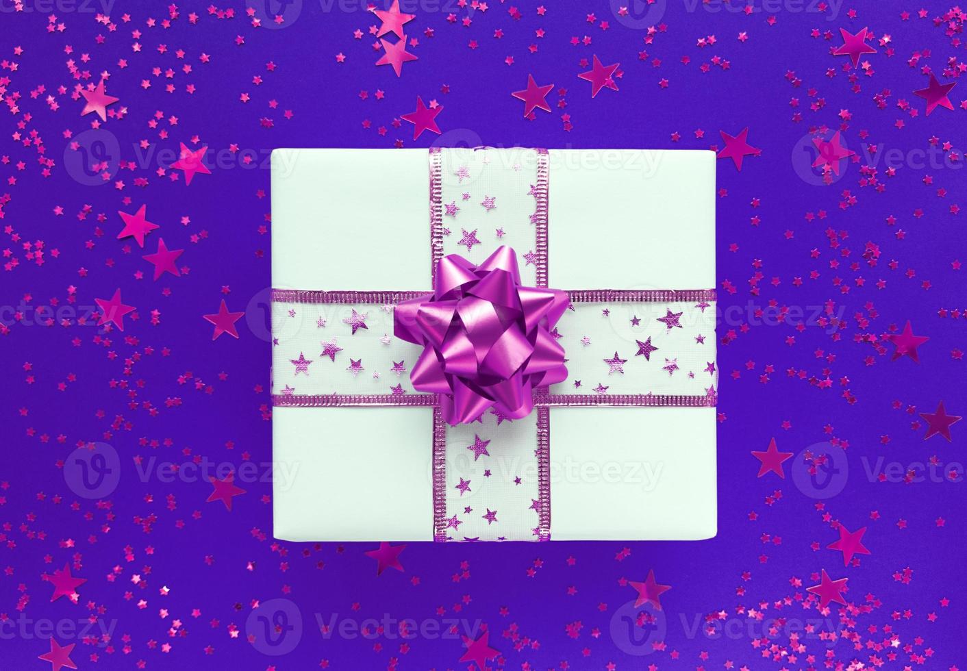 weiße Geschenkbox mit rosa Schleife und Sternen auf violettem Grund foto