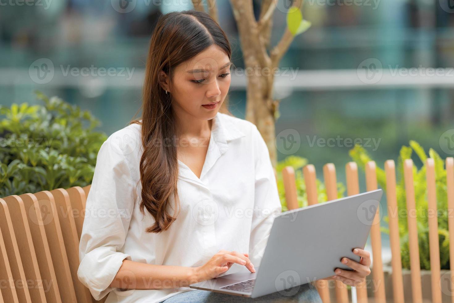 junge asiatische Frau sitzt mit Smiley-Gesicht mit Laptop in einer Stadt foto