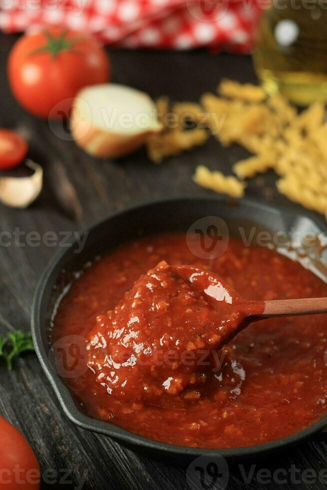 Tomate Soße mit hölzern Löffel im Besetzung Eisen Bratpfanne schwenken foto