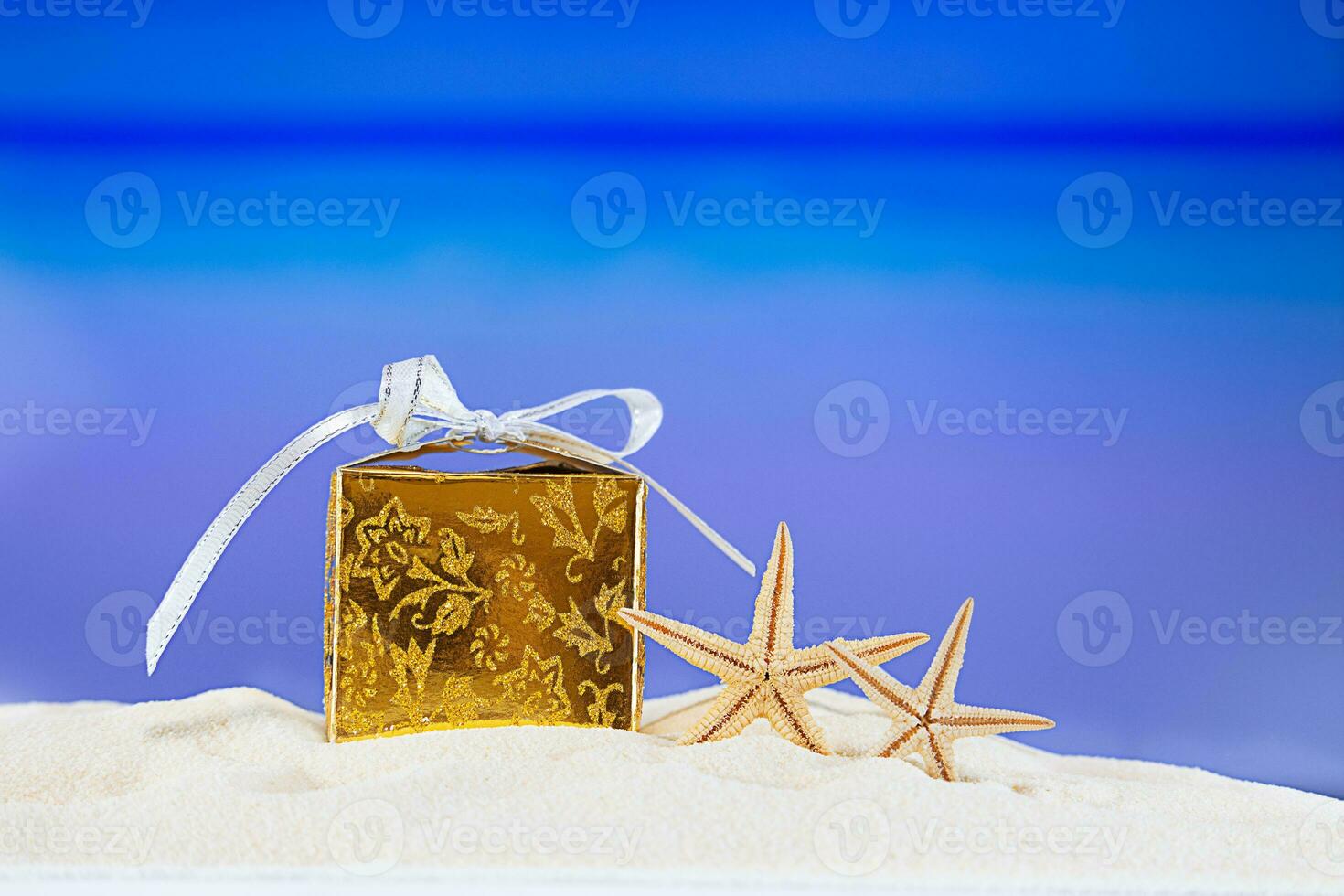 golden verpackt Geschenk Box mit Gelb Sterne beim tropisch Ozean Strand. Weihnachten, Neu Jahr, Geburtstag Ferien im heiß Länder Hintergrund Konzept. Kopieren Raum foto