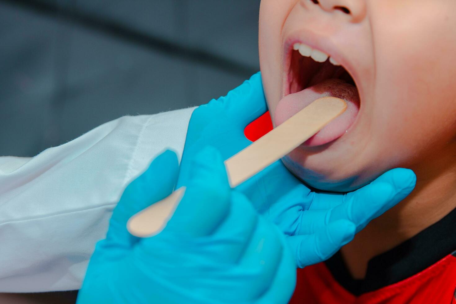 das Arzt Verwendet ein Zunge depressor zu untersuchen das Kinder Zunge. foto