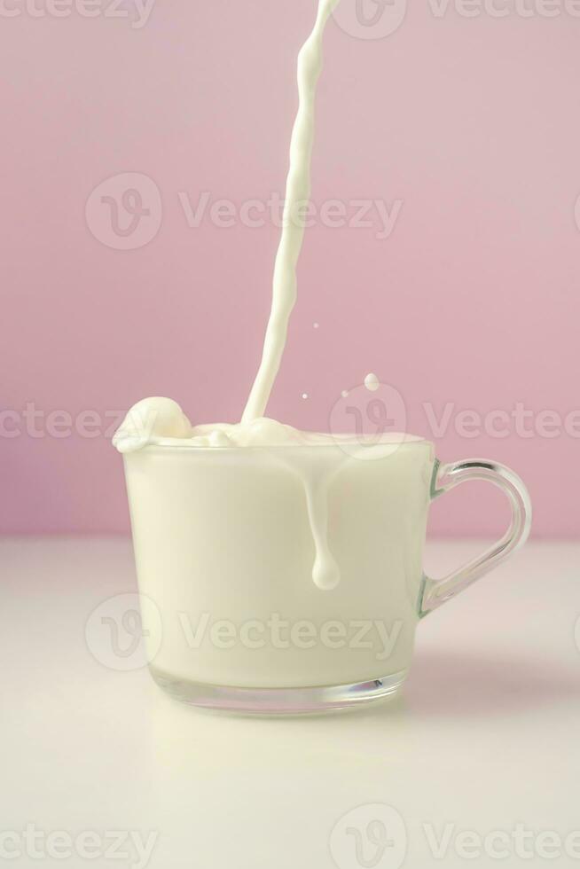 Milch ist gegossen in ein transparent Tasse auf ein lila Hintergrund. foto