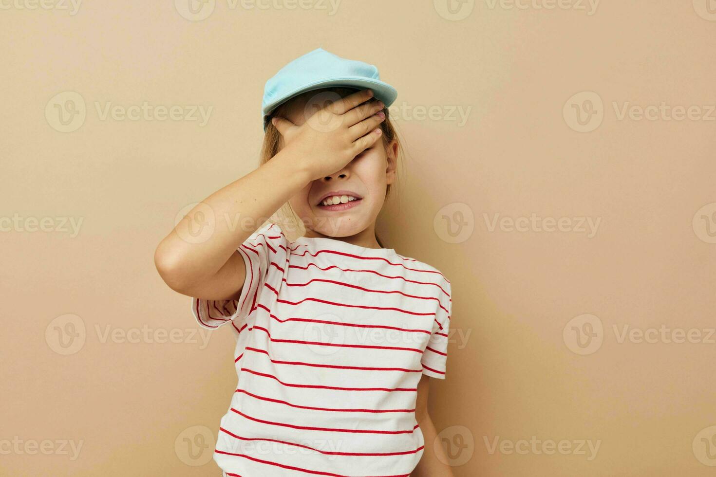 Porträt von glücklich lächelnd Kind Mädchen im Blau Kappen gestreift T-Shirt Emotionen Beige Hintergrund foto