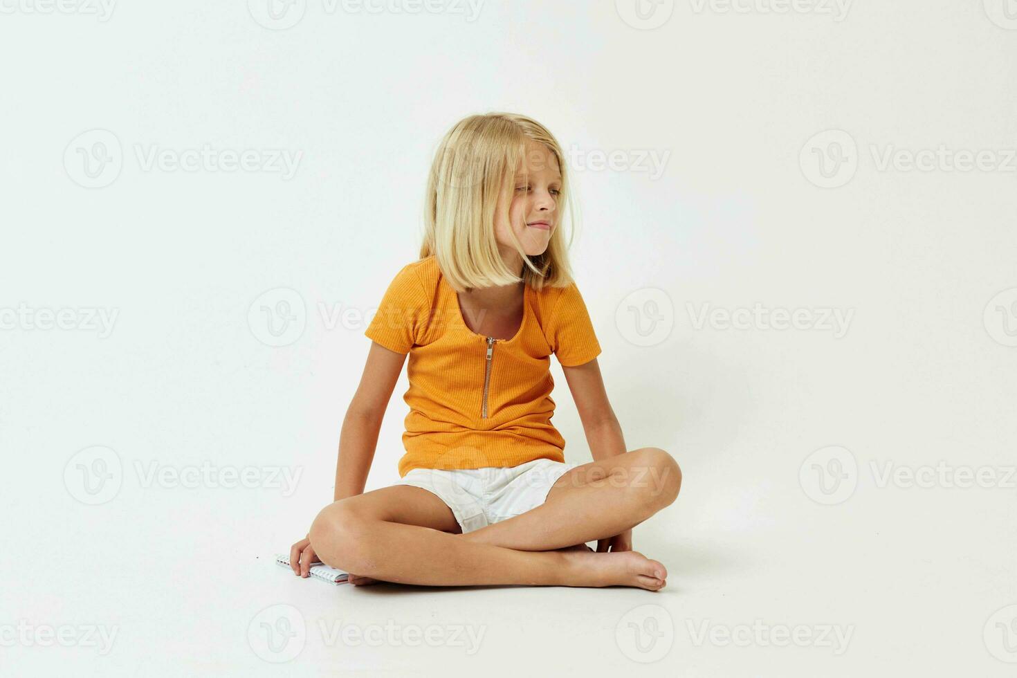wenig Mädchen mit blond Haar gestikulieren mit ihr Hände während Sitzung auf das Fußboden foto