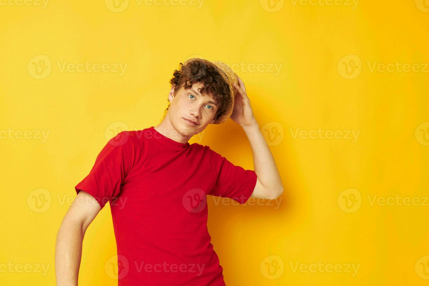 Porträt von ein jung lockig Mann im ein rot T-Shirt mit ein Mode Hut Lebensstil unverändert foto