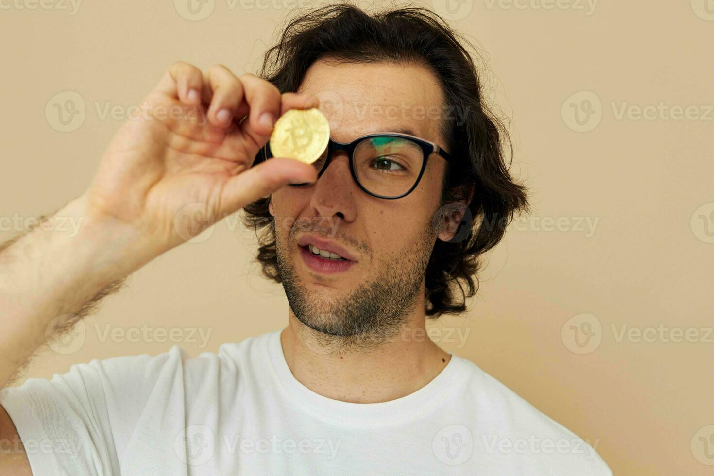 heiter Mann mit Brille Gold Bitcoin im Hände Beige Hintergrund foto