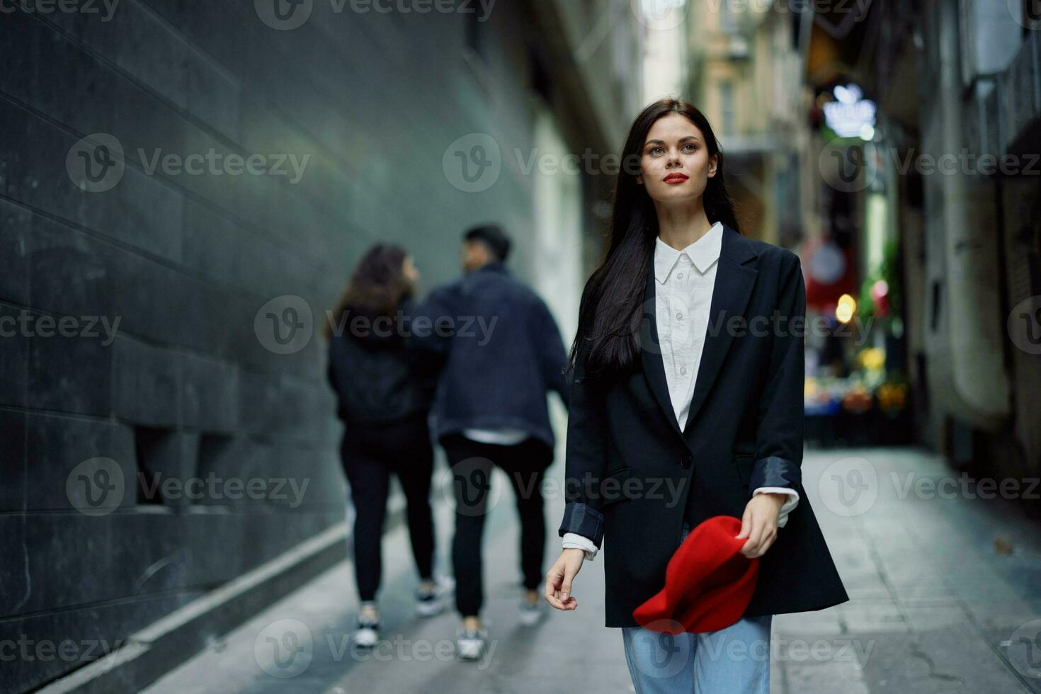 Mode Frau Tourist im stilvoll Kleider im ein Jacke und rot Baskenmütze Gehen Nieder ein eng Stadt Straße fliegend Haar und glücklich reisen, Französisch Stil, filmisch Farbe, retro Stil. foto