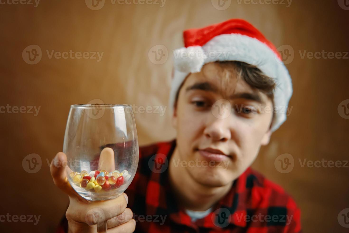 Kerl mit Weihnachtsmann-Hut hält ein Glas mit verschiedenen Pillen foto