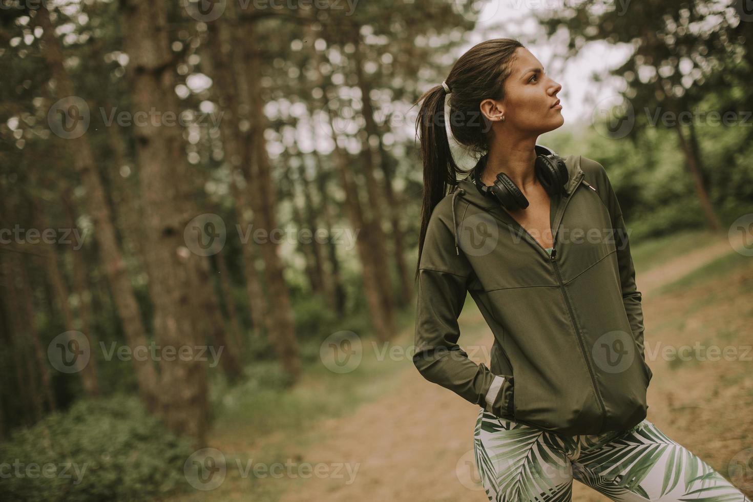 junge schöne Läuferin, die Musik hört und eine Pause macht, nachdem sie in einem Wald joggt foto