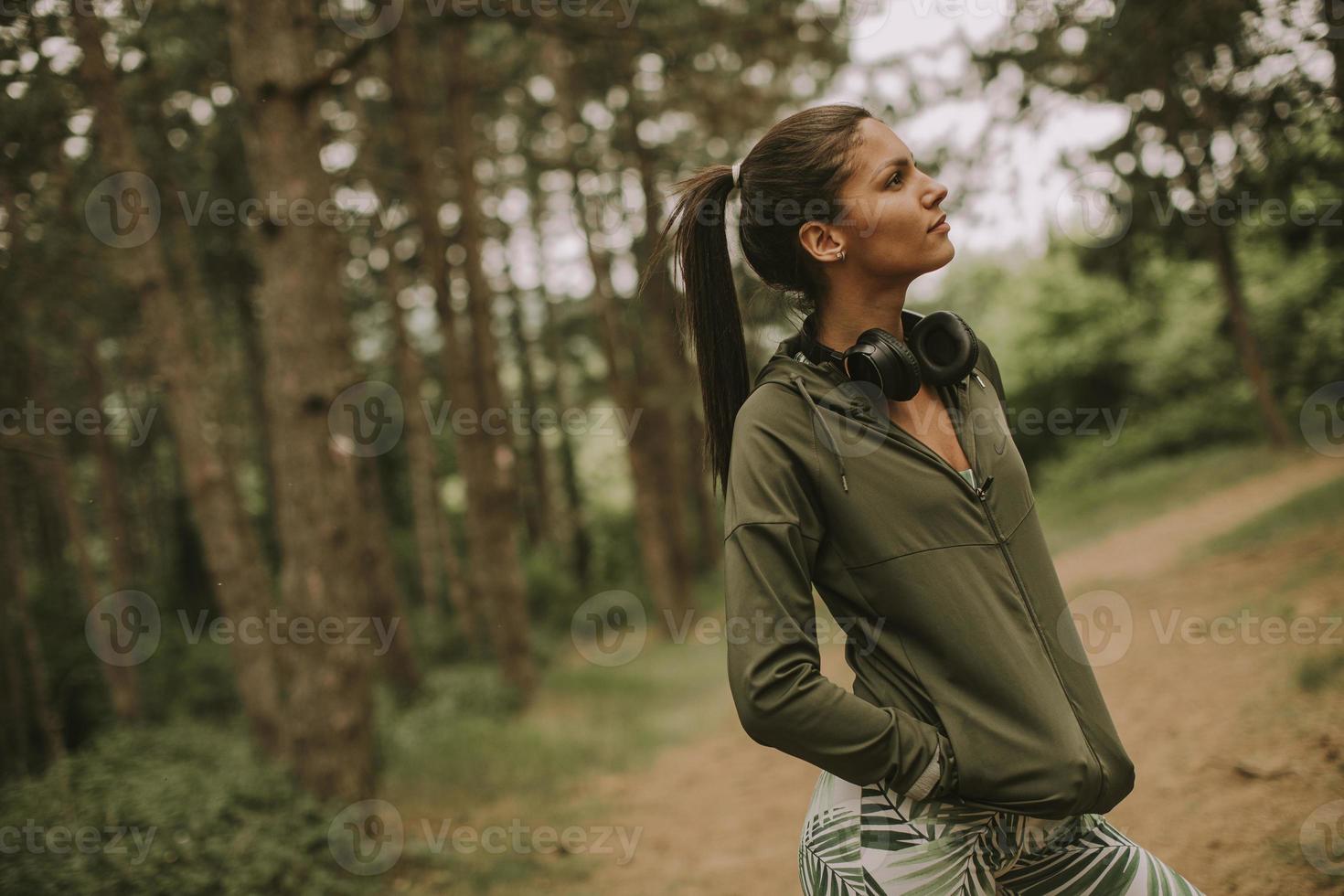 junge schöne Läuferin, die Musik hört und eine Pause macht, nachdem sie in einem Wald joggt foto