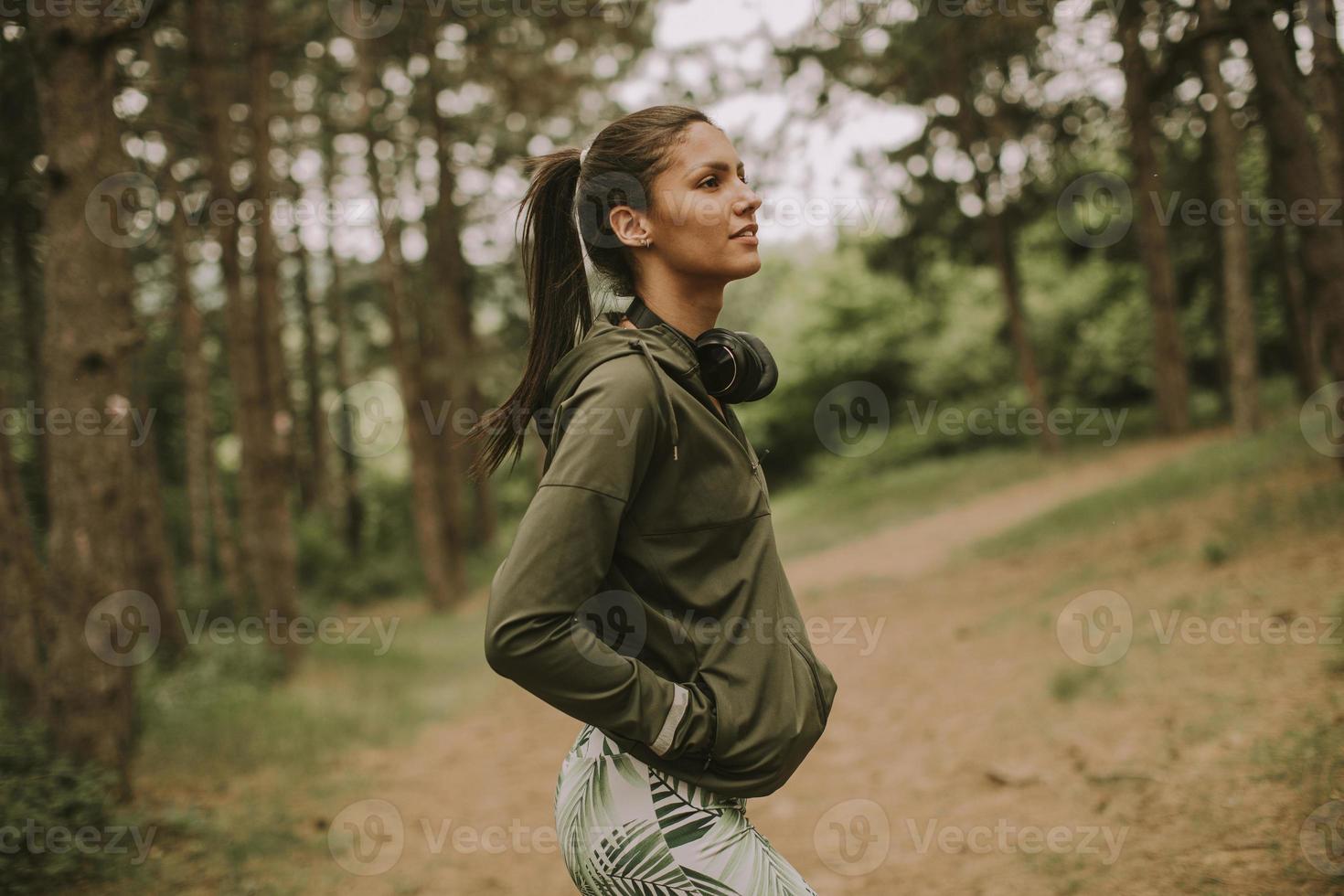 junge schöne Läuferin, die Musik hört und eine Pause macht, nachdem sie in einem Wald joggt foto